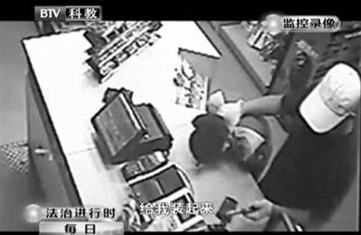 戴帽男子一手掐住加油站營(yíng)業(yè)員，一手持發(fā)令槍指向另一營(yíng)業(yè)員，要求“把錢給我裝起來(lái)”。