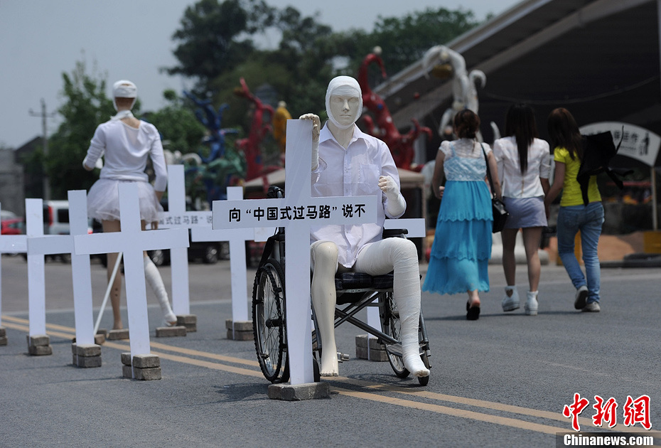 4月16日，重慶市洋人街上擺放著兩個受了傷的塑料人像“模特”，旁邊十字架上寫著向“中國式過馬路”說不