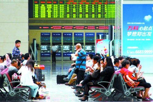 候車大廳溫度很高，一名乘客一手扇風(fēng)、一手擦汗