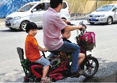周先生騎著一輛低矮的電動(dòng)車帶著一對兒女，很不安全。