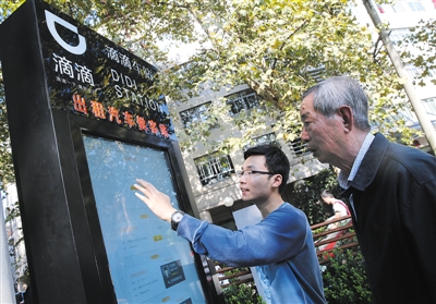 10月15日，滴滴工作人員（左）指導(dǎo)乘客使用“滴滴車站”的電子屏預(yù)約出租車。