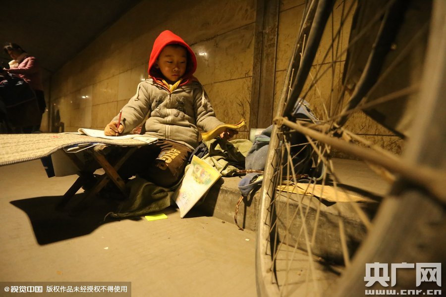 2015年11月8日晚，鄭州，7歲男孩涵洞橋下陪父母練攤，路邊燈下坐小馬扎上寫作業(yè)。