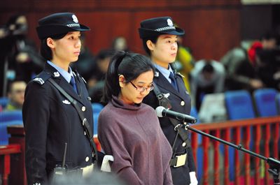 被告人盧梅低著頭，站在朝陽(yáng)法院刑事審判庭的被告席上。