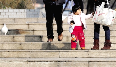 昨天中午，一女孩拉著家長(zhǎng)的手在紫荊山公園曬太陽，氣溫升高，孩子的棉衣解開了扣子。