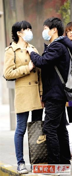 公交站臺上，一對年輕人戴著口罩，系緊衣領(lǐng)。